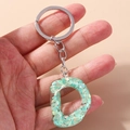 Close-up of letter D keychain with mint green resin and silver ring held by hand - Letter D