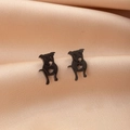 Detailed close-up of cute black pug puppy stud earrings on pink satin fabric background - Black