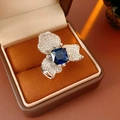 Vista macro de un anillo plateado vintage con circón azul cuadrado y detalles florales - Anillo Abierto de Flor / Plata-Azul