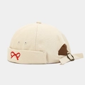 Detail of beige brimless docker cap featuring red bow embroidery and adjustable metal buckle - Beige