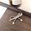 Silver bow hair claw with pearl pendants and 5cmx3cm dimensions on wood surface - Gray
