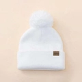 Detalle de un gorro de punto blanco con pompón y parche de cuero con texto FASHION - Blanco