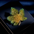 Elegant gold maple leaf brooch with green crystal pavé setting on a blue jewelry box - Yellow-Green