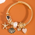 Gold cable bangle with starfish, shell, pearl and turtle charms on a warm background - Black