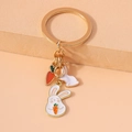 Detailed macro view of a gold-tone metal keychain featuring white enamel rabbits and carrots - Carrot Rabbit