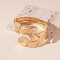 Detail shot of golden metal leaf bracelet with embossed veins on a stone pedestal - Gold