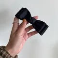 Elegant black satin double-layered bow hair clip shown held in hand for hair styling - Black
