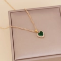 Golden heart necklace with emerald zircon and diamond halo on beige jewelry box - Green