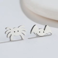 Macro shot of silver asymmetrical punk stud earrings featuring a spider and bat design - Steel