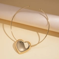 Detailansicht eines glänzenden goldenen Herzanhängers am Choker auf beigem Sockel - Gold Herz Stil