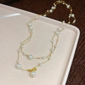 Detail of a double-layered gold necklace with irregular white pearls on a soft tray - Necklace - Gold - White