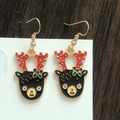 Close-up of Christmas reindeer earrings with red antlers and green bow on wooden backdrop - Cartoon Black Reindeer Face