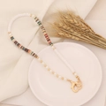 Close-up of Bohemian clay bead necklace with pearls and golden heart clasp on white linen - Brown Multi