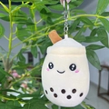 Close-up of a plush milk tea cup keychain with embroidery, hanging on green leaves - 11cm / Beige