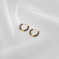 Detail von goldenen Creolen mit schwarzen Emaille-Spiralen auf weißem Seidenhintergrund - Schwarz
