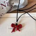 Close-up of polished red bow pendant on a black cord over a neutral textured surface - 17# Necklace - Red-Bowknot Ribbon