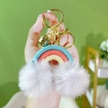 Bohemian rainbow keychain with sky blue pom-poms and gold clasp held in hand - Lake Blue