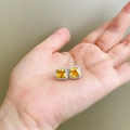 Close-up of square yellow gemstone earrings with white diamond halo on a palm - Square Golden Yellow Zircon Studs