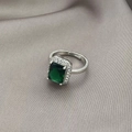 Macro-opname van smaragdgroene ring met zirkonia halo op een grijze zijden achtergrond - Verstelbaar Open / Smaragd