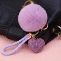 Purple plush ball keychain with rhinestone heart charm and woven strap on black bag - Rhinestone Heart + Violet Pom
