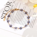 Detail of a gold stainless steel chain bracelet with blue enamel daisy charms and lobster clasp - Blue