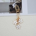 Golden flower keychain with three white five-petal pendants on a textured background - White