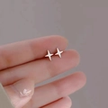 Macro shot of minimalist silver four-point star stud earrings held on a fingertip - Cross / Silver