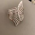 Close-up van een zilveren brede manchetarmband met gelaagd vleugelachtig golfontwerp - Vleugel Holle Open Stijl / Zilver