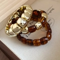 Close-up of retro acrylic and gold beaded bracelets in a beige jewelry display box - Amber (Set)