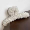 Close-up of white plush lamb wool hair claw clip on dark wooden surface background - Milk White