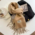 Beige cashmere style scarf with tassels and black tweed jacket on a white table - Camel Grey