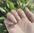 Close-up of glossy nude almond-shaped press-on nails shown on hand against nature background - Nude Apricot Oval (CW516)