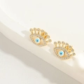 Close-up of golden evil eye stud earrings with blue enamel and sparkling zircon accents - White Eyelash