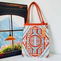 Close-up of geometric knit tote bag in orange and blue with YOU ONLY LIVE TWICE tag - New Chinese Orange