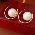 Dettaglio macro di orecchini vintage a forma di C dorata con una grande perla bianca tonda - Stile con perno dell'orecchino in argento / Oro - Champagne