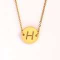 Détail macro du pendentif rond en acier inoxydable doré avec lettre H ajourée - Lettre H