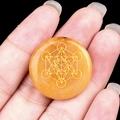 Orange crystal disc featuring golden Metatron Cube geometry held in hand - Topaz