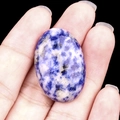 Polished blue and white sodalite oval stone displayed on a palm for size reference - Sodalite