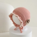 Detail of pink knitted baby bonnet with white ruffled edges and delicate flower accent - 6-24 Months / Pink