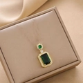 Elegante colgante verde esmeralda con base dorada sobre una caja de regalo beige con textura - Solo Colgante / Esmeralda