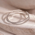 Detailweergave van een zilveren meerlaagse zirkonia armband op een stenen blad - Kruis Open Armband / Zilver