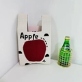 Close-up of knit tote bag with red apple pattern and pink book inside on white surface - Beige Apple