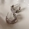 Elegant C-shaped twisted earrings with pavé cubic zirconia on a cream ceramic plate - Twisted C-Shape Style / Silver