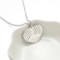 Detail van hartvormige garenbal hanger aan O-ketting gepresenteerd in wit keramiek schaaltje - Liefde Hart Staal