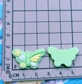 Detailed macro view of light green resin butterfly charms with floral texture on a ruler pad - Green