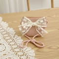 Detailed view of pink woven crossbody bag with large white lace bow on wooden surface - Bag-Pink