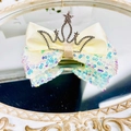 Detail of glitter sequins bow hair clip with silver crown on a decorative mirror surface - Beige