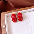 Detail view of oval dark red stud earrings in gold base on white jewelry box padding - Red (Gold Base with Silver Pin)