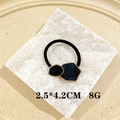 Detail view of black geometric hair tie with gold trim on a white stone background - Enamel Marble Black