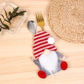 Macro view of Christmas gnome cutlery holder with red striped hat on a rustic table - Striped